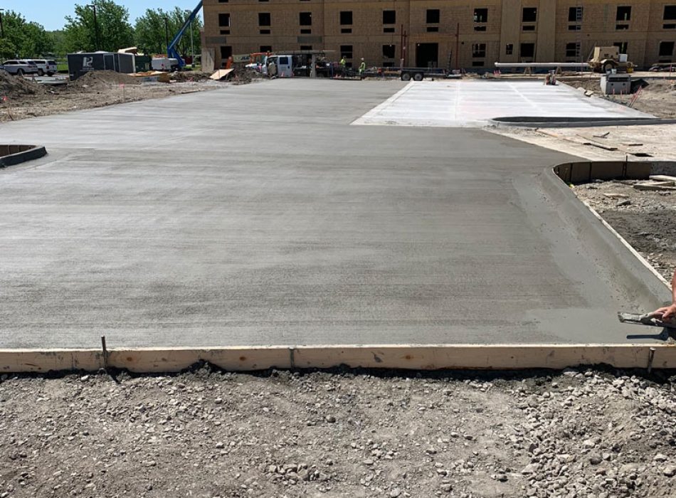 Concrete flatwork being laid in front of an in-construction hotel.