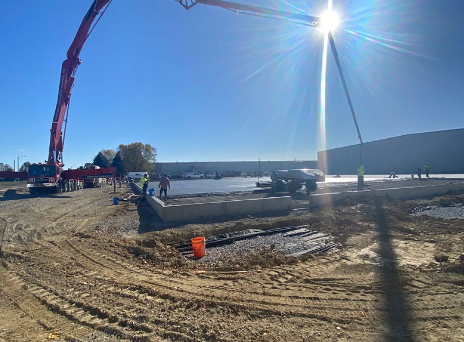 Concrete flatwork being laid with a boom pump. The sun is shining brightly at one of the arms of the boom pump.