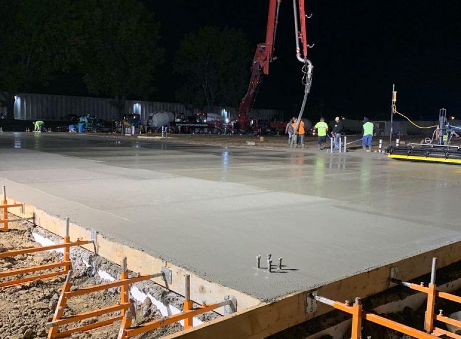 Concrete flatwork being laid by a boom pump at night.